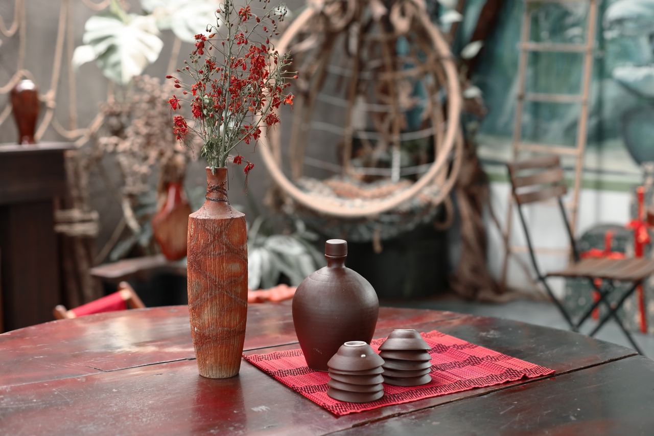 Warm rustic still life with ceramic vases and dried flowers on a red mat indoors.
