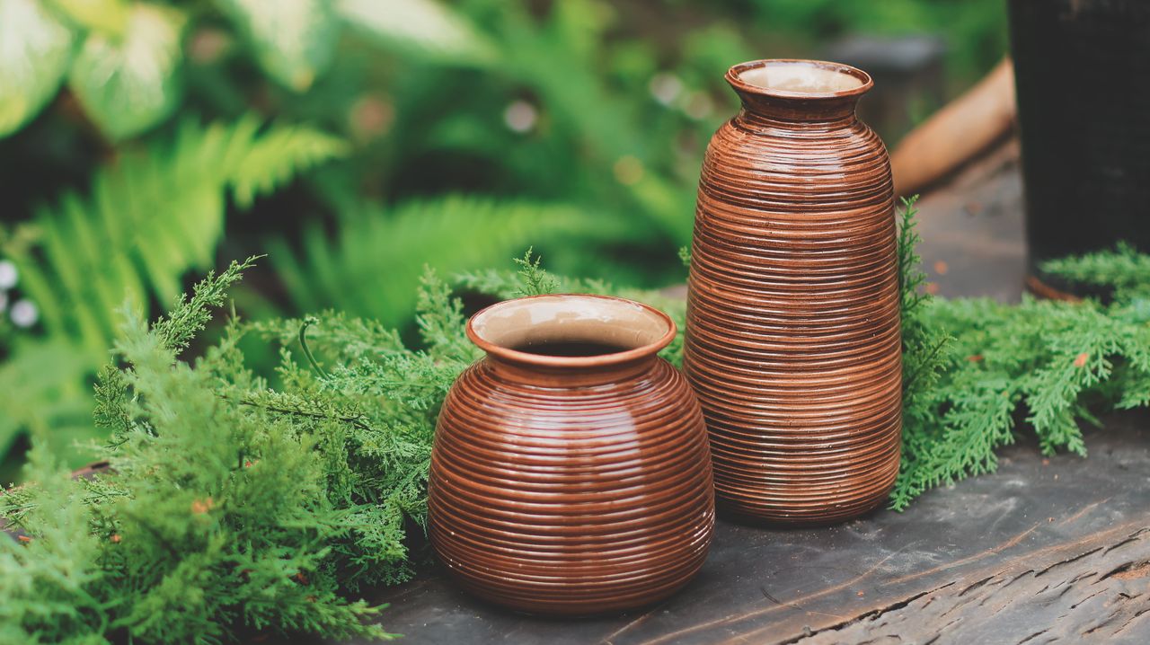 Two ribbed brown vases surrounded by lush greenery create a rustic aesthetic.