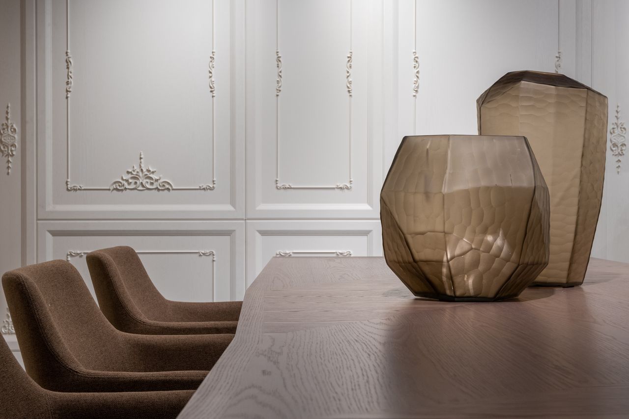 Stylish creative vases placed on dining table near cozy armchairs in light classic dining room